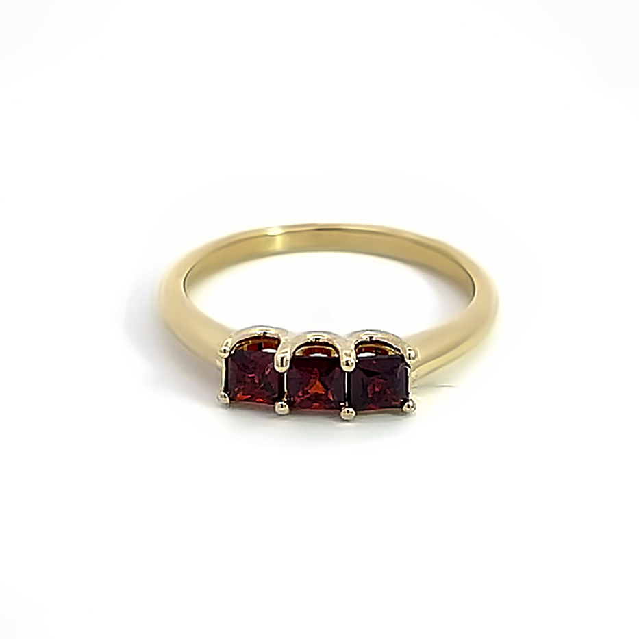three princess cut garnets on yellow gold band on white background
