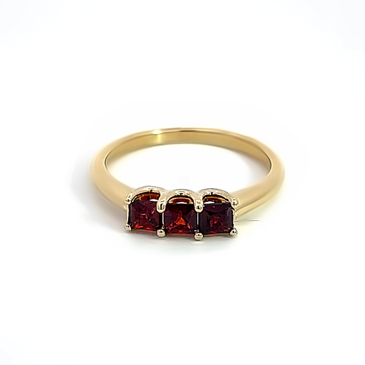 three princess cut garnets on yellow gold band on white background