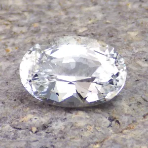 Loose oval cut white topaz gemstone, 5.16 carats, water-clear and colorless, photographed on neutral stone surface.